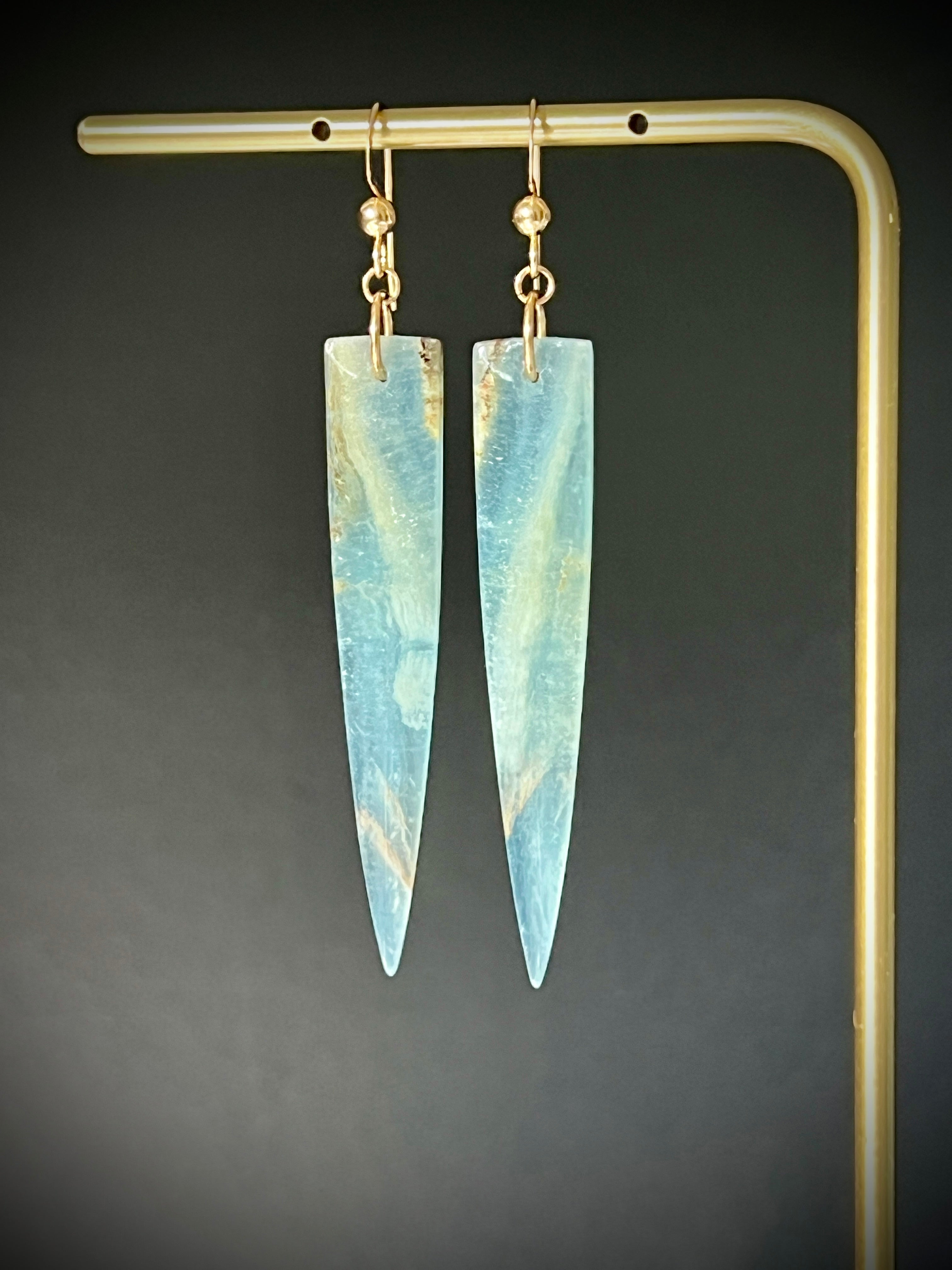Lemurian Calcite dagger earrings in 14K gold fill hanging on a brass display 