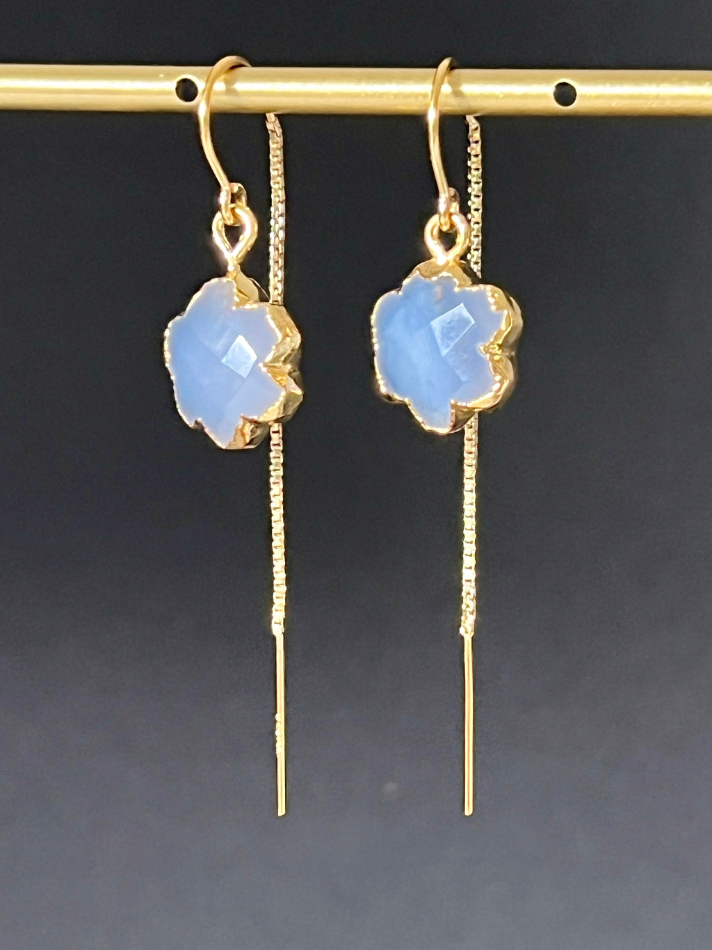 Pair of blue chalcedony flower threader earrings in 14K gold fill hanging on a gold bar, dark background, showing faceted pale blue stone and long box chain drop by Studio MS Indie Jewlery