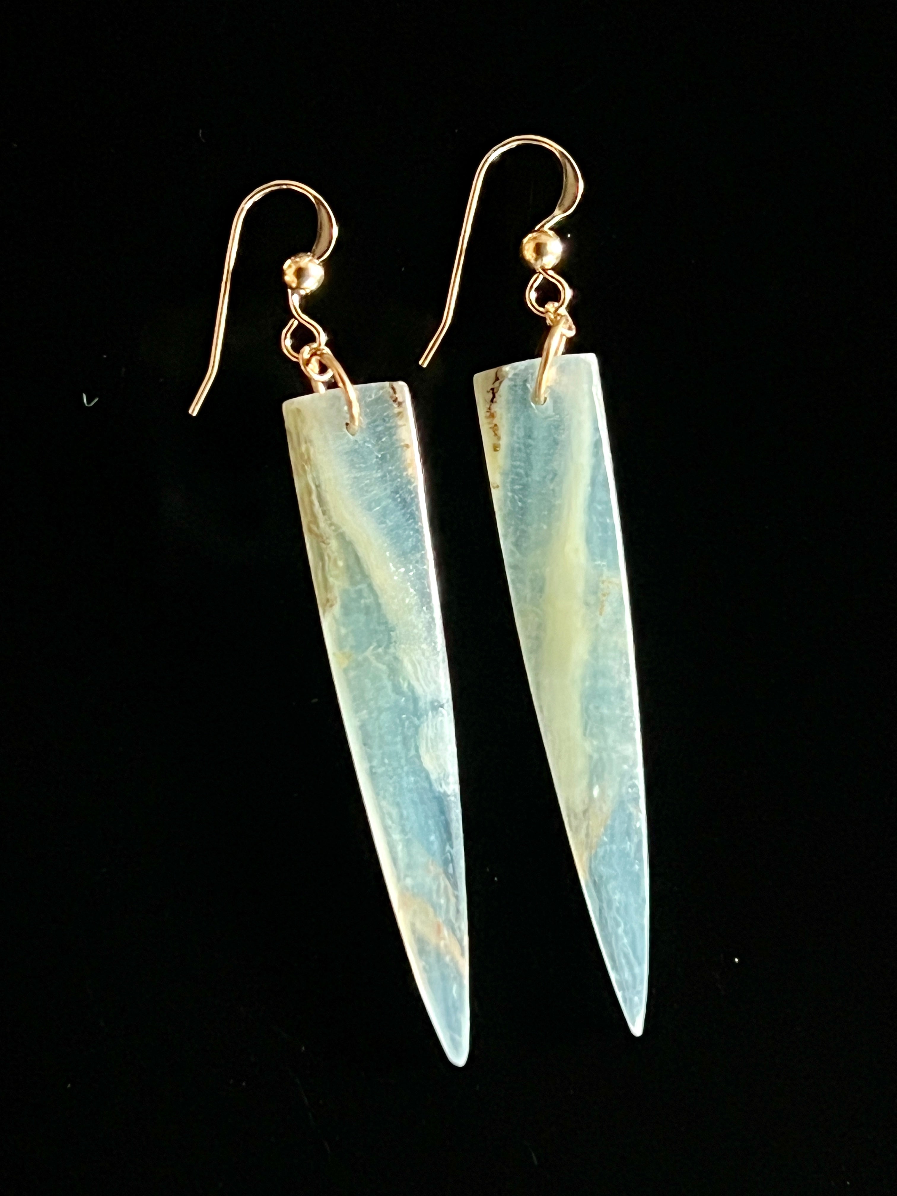 Pair of Lemurian Calcite dagger drop earrings with 14K gold fill fish hook wires on a black background, highlighting the stone's soft blue and amber mineral detail