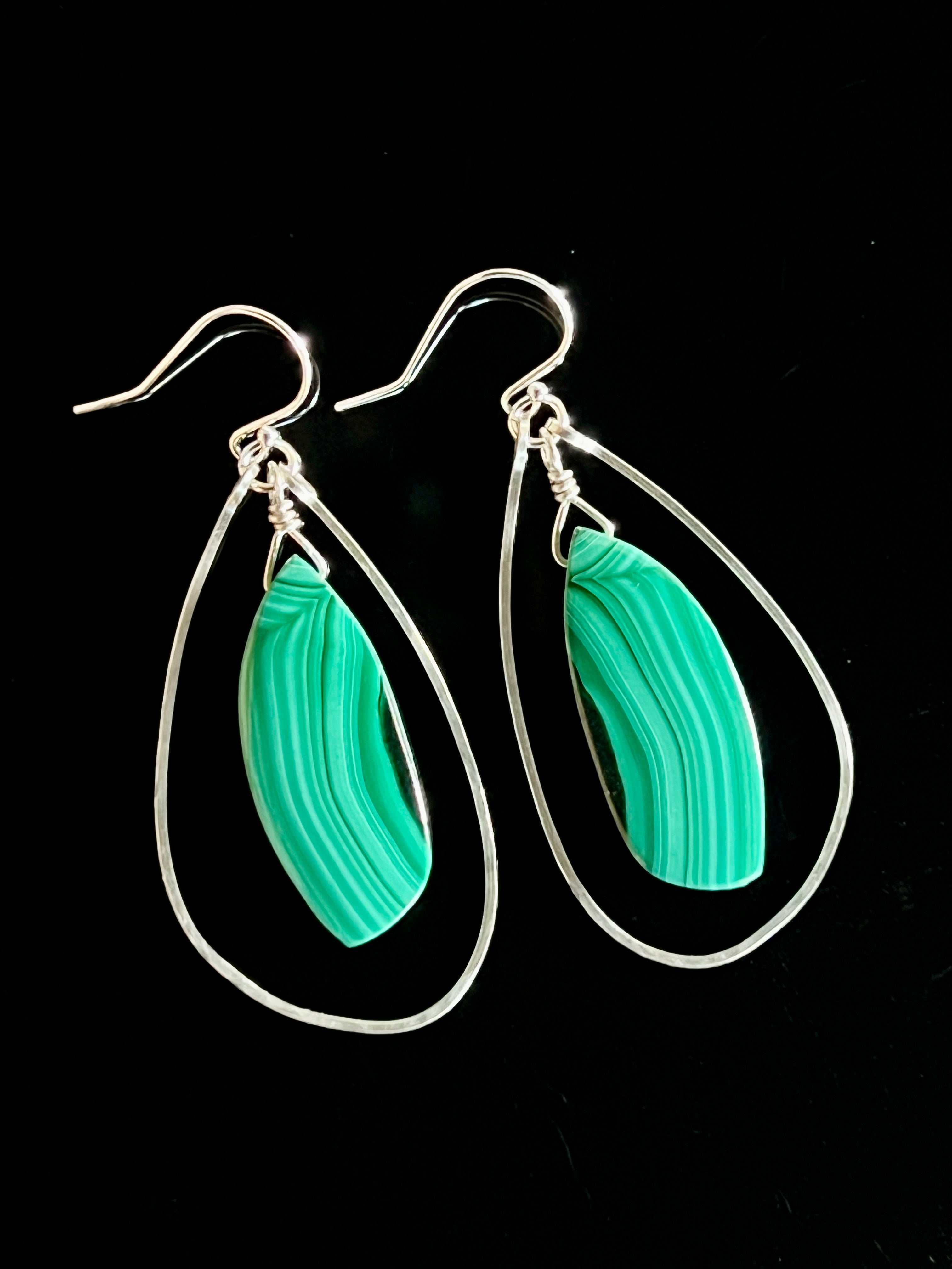 Pair of malachite and sterling silver freeform dangle earrings on a black background, showing vivid green banded marquise stones suspended inside open teardrop wire frames with fish hook wires