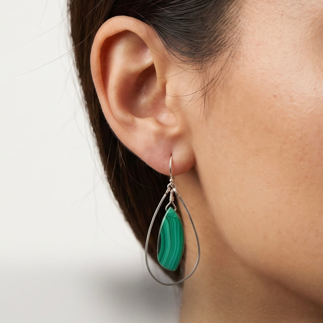 Malachite and sterling silver freeform dangle earring worn on a model with dark hair, showing a marquise malachite stone with deep green banding inside a hand-formed silver teardrop frame