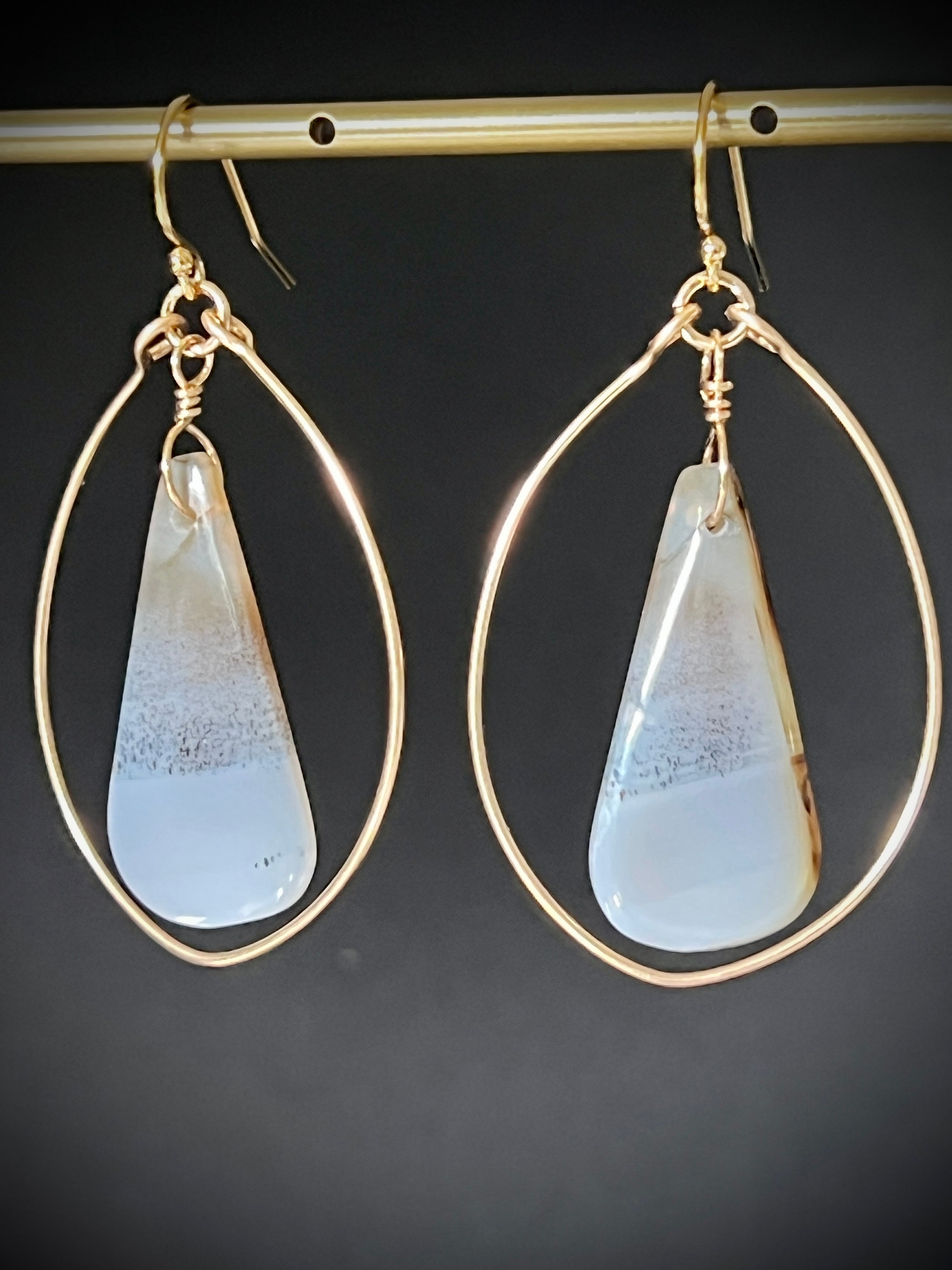Pair of Montana agate dangle hoop earrings in 14K gold fill hanging on a gold bar, dark gray background, showing translucent freeform stones inside hammered teardrop gold wire frames by Studio MS Indie Jewelry