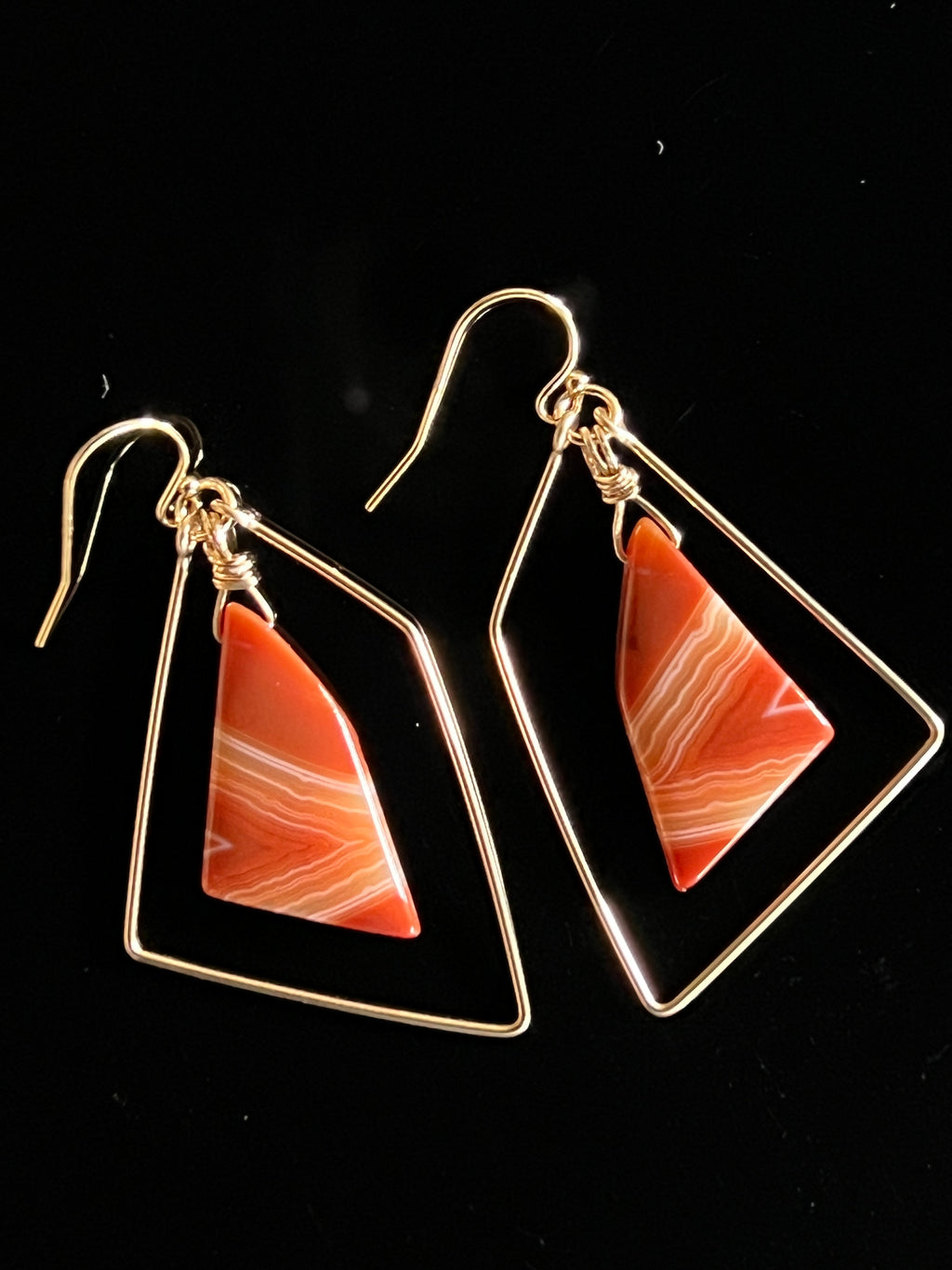 Pair of sardonyx freeform earrings in 14K gold fill on black background, showing vivid orange and cream banded stones inside angular hammered gold wire frames