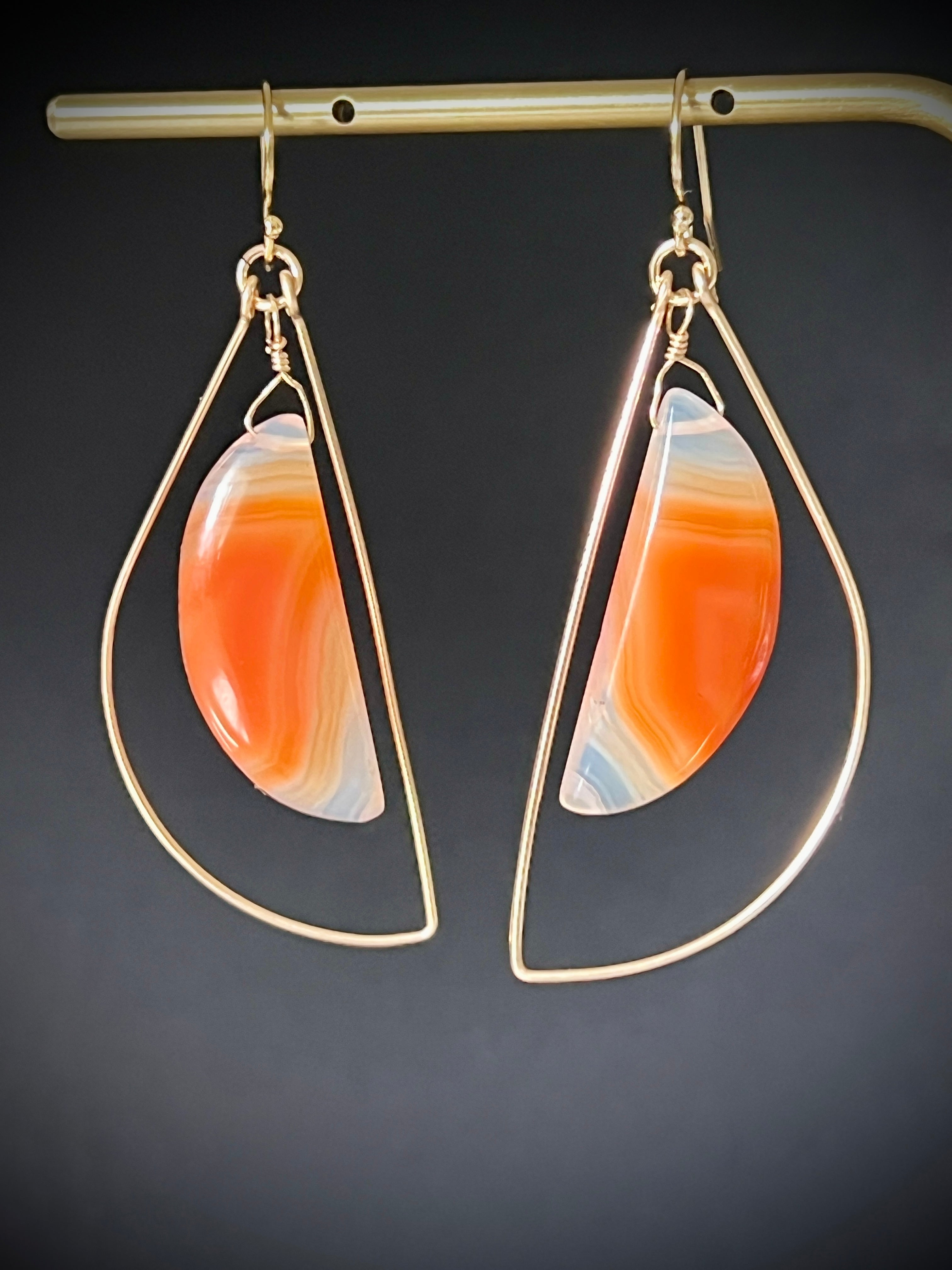 Sardonyx freeform dangle earrings in 14K gold fill hanging on a gold bar, dark gray background, showing vivid orange banding